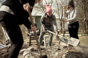 osoby pracują w ogrodzie, za pomocą łopat przerzucają ziemię