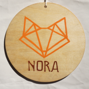 Drewniana zawieszka z linearnym pomarańczowym lisem i podpis 'NORA'