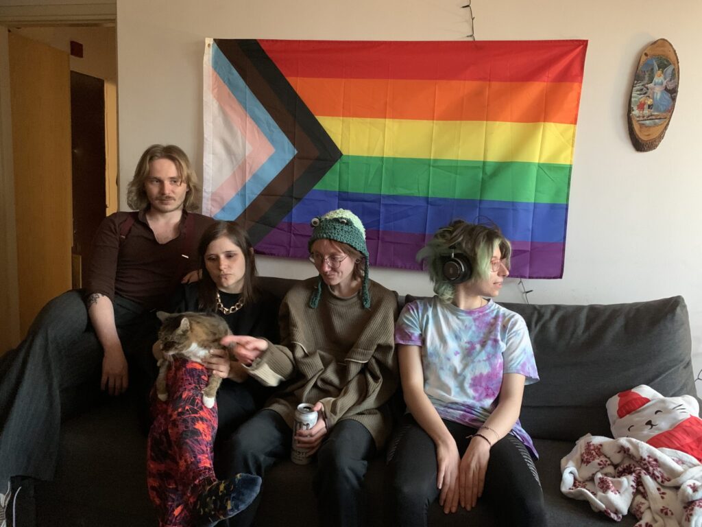 Osoby na kanapie na tle flagi LGBTQ plus